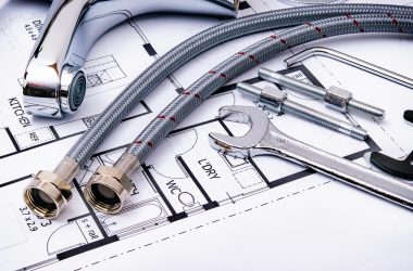Close-up of plumbing tools and faucet on top of an architectural blueprint, perfect for hardware and construction themes.