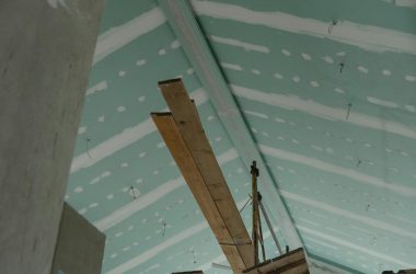 Scaffolding setup in an interior construction space with suspended ceiling boards and wooden planks.