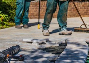 Workers laying tiles on an outdoor patio under sunlight.