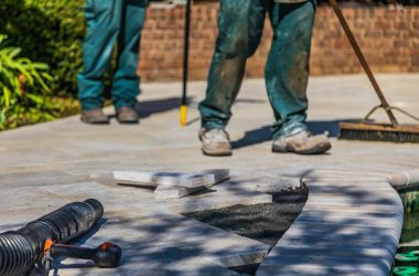 Workers laying tiles on an outdoor patio under sunlight.